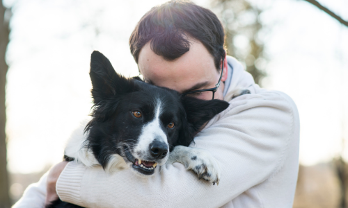 A dog owner hugging their dog outdoors on a clear day.